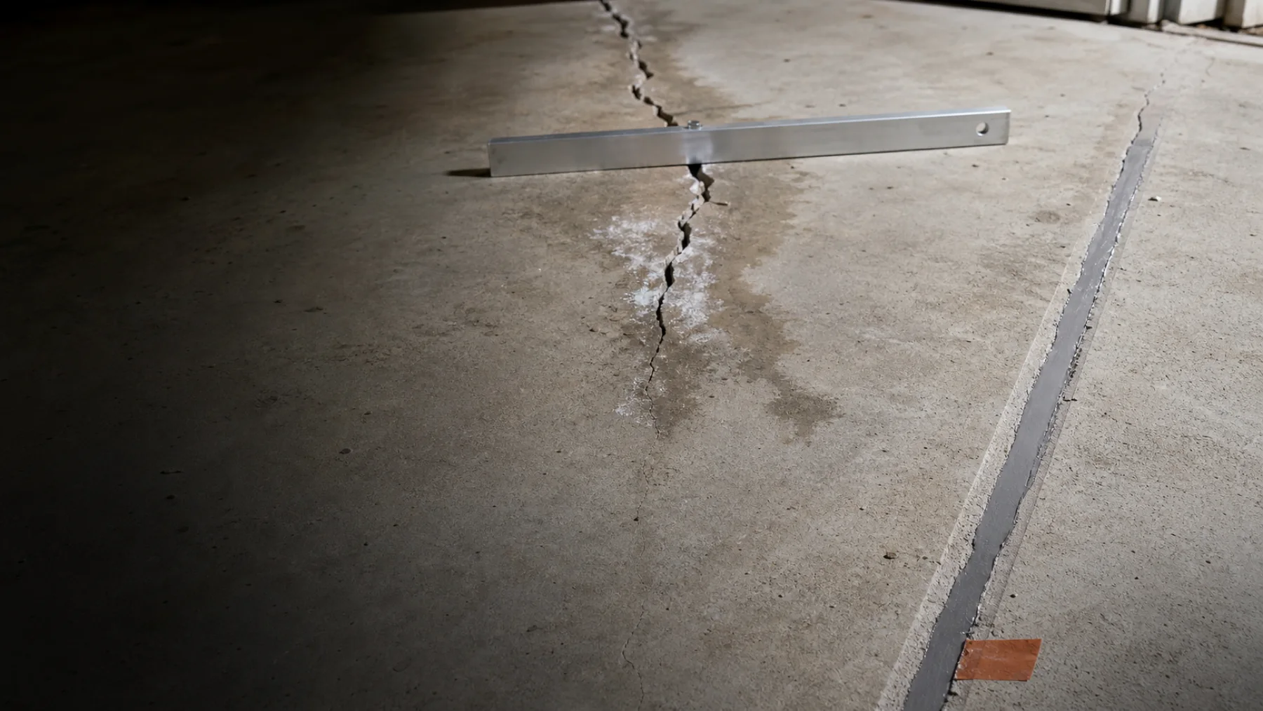 Stable repaired crack and a separate displaced moisture-stained crack in the same garage slab.